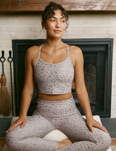 woman in pink mini moon printed cropped tank and leggings sitting on a yoga mat in front of a fireplace.