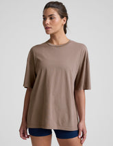 model wearing a brown oversized cotton t-shirt and navy shorts on a light gray background.