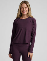model wearing a purple scoop neck long-sleeve top and leggings on a light gray background.
