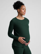model wearing a green maternity crew neck long-sleeve top and leggings against a light gray background.