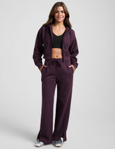 model wearing a purple fleece zip-up jacket and purple fleece wide leg pants with slits on side and a drawcord at waistband on a white background.