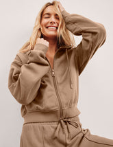 person wearing a brown fleece zip-up jacket and fleece pants against a plain background.