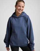 woman wearing a blue hoodie and black sweats against a plain background.