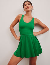 green mini dress in our stretch woven fabric with stitch down front pleats, a scoop front neckline, open back detail, bodice in performance stretch fabric, and skirt side vents for easy pocket access.