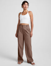 Woman wearing a white tank top and brown high-waisted trousers on a light gray background