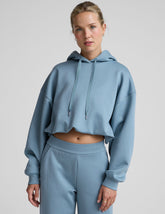 woman wearing a light blue hoodie and matching pants on a plain background.