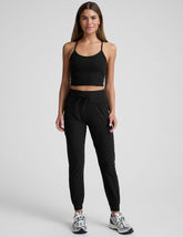 model wearing a black cropped tank and black high-waisted midi length joggers with a drawcord at waistband and pockets against a plain background.