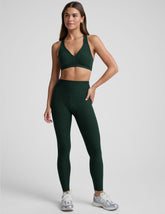 model wearing a green athletic bra and green high-waisted full length leggings on a plain background.