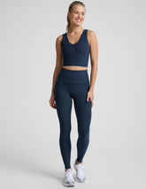 woman is wearing a blue v-neck cropped tank and blue high-waisted midi length leggings against a plain background.