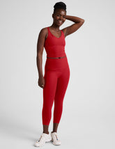 woman wearing a red cropped tank and capri length leggings on a plain background.