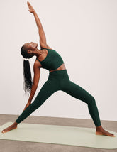 person in green slim racerback cropped tank and leggings performing a yoga pose on a mat.