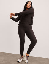 woman wearing a brown long sleeve and high-waisted midi length pocket leggings  with a plain background.