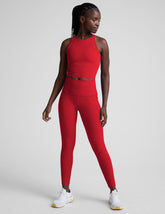 woman wearing a red cropped tank and high-waisted midi length pocket leggings on a plain background.