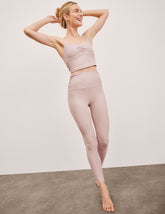 model wearing a pink cropped tank top and pink high-waisted midi length leggings on a plain background.