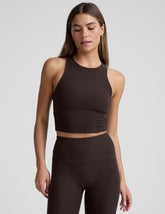 woman wearing a brown high neck racerback cropped tank and leggings on a plain background.