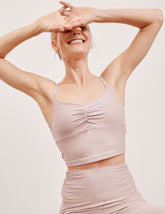 model wearing a pink cropped tank top with shirring at center front and pink high-waisted midi length leggings against a plain background.