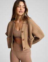 woman wearing a brown button up ribbed cardigan against a plain background.