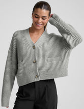 woman wearing a gray ribbed cardigan on a plain background.