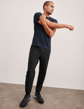 man wearing a navy t-shirt and black joggers standing against a plain background.