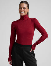 model wearing a red turtleneck long sleeve top and black pants on a plain background.