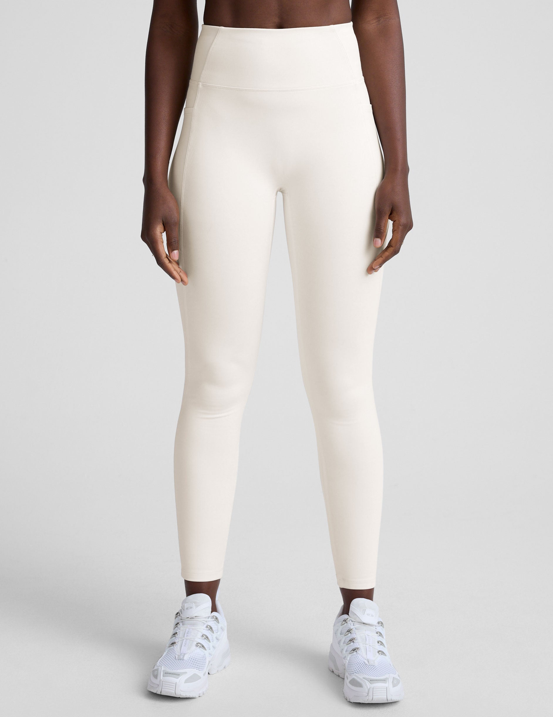 woman wearing white high-waisted long length leggings with pockets on a plain background.