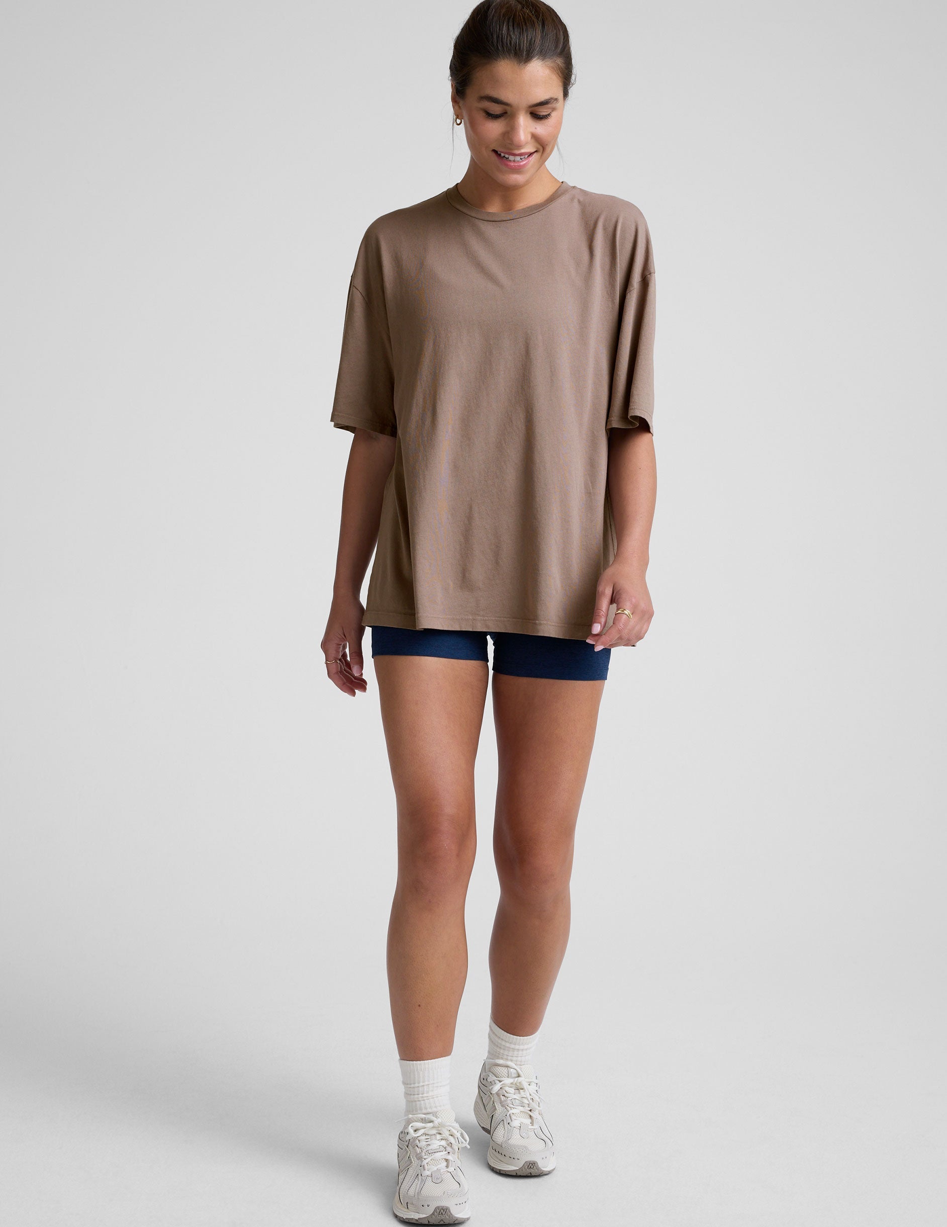 model wearing a brown oversized cotton t-shirt and navy shorts on a light gray background.