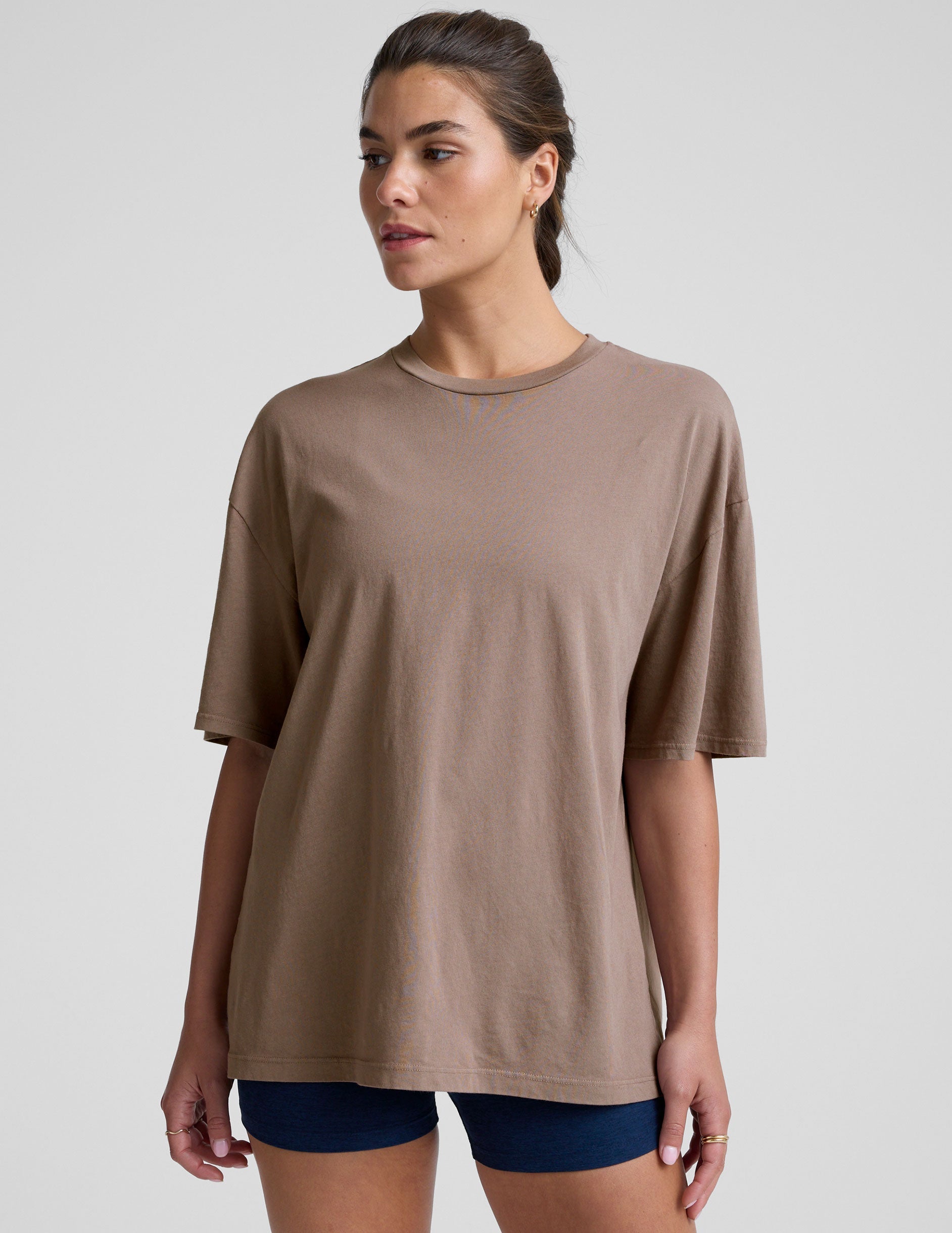 model wearing a brown oversized cotton t-shirt and navy shorts on a light gray background.