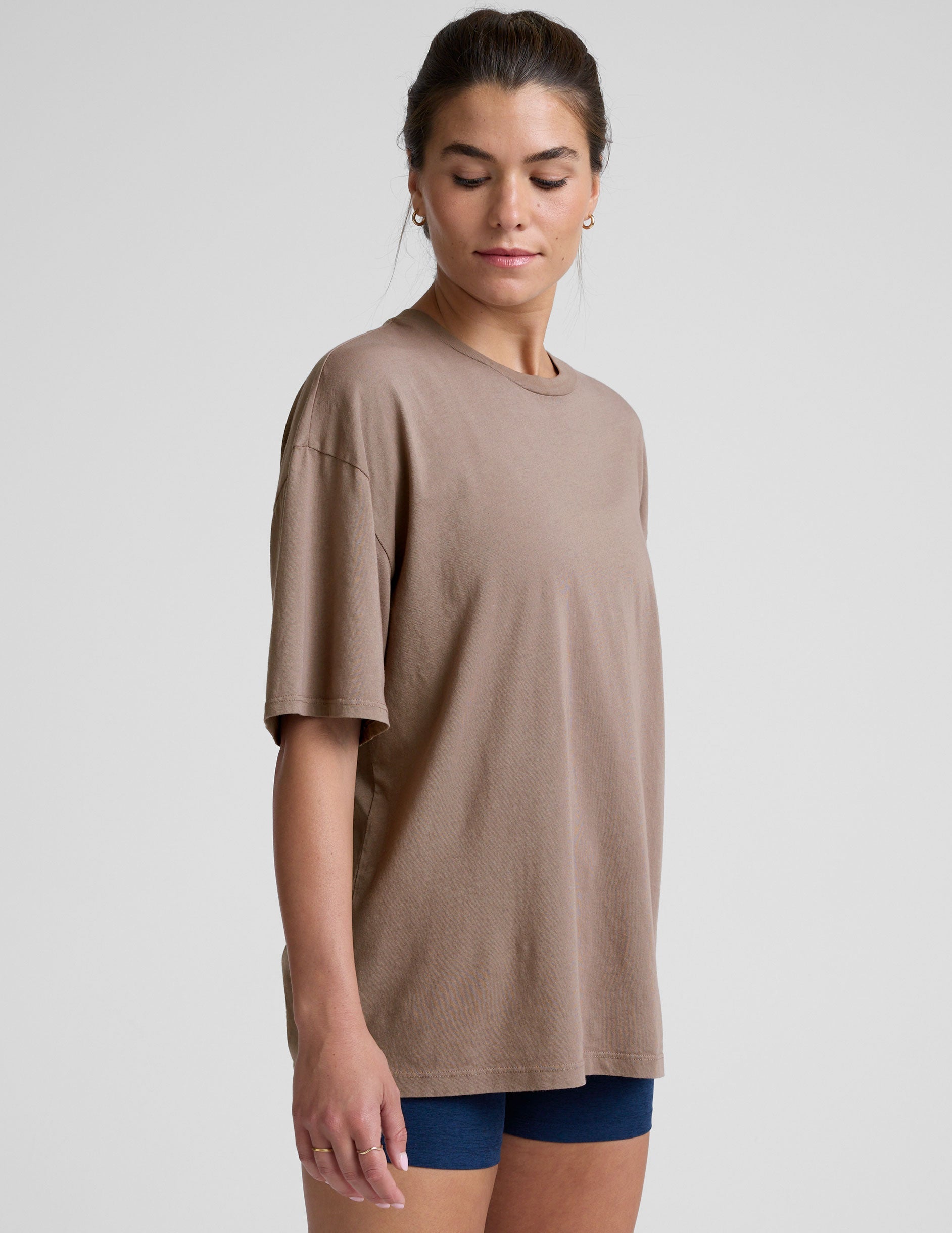 model wearing a brown oversized cotton t-shirt and navy shorts on a light gray background.