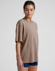 model wearing a brown oversized cotton t-shirt and navy shorts on a light gray background.