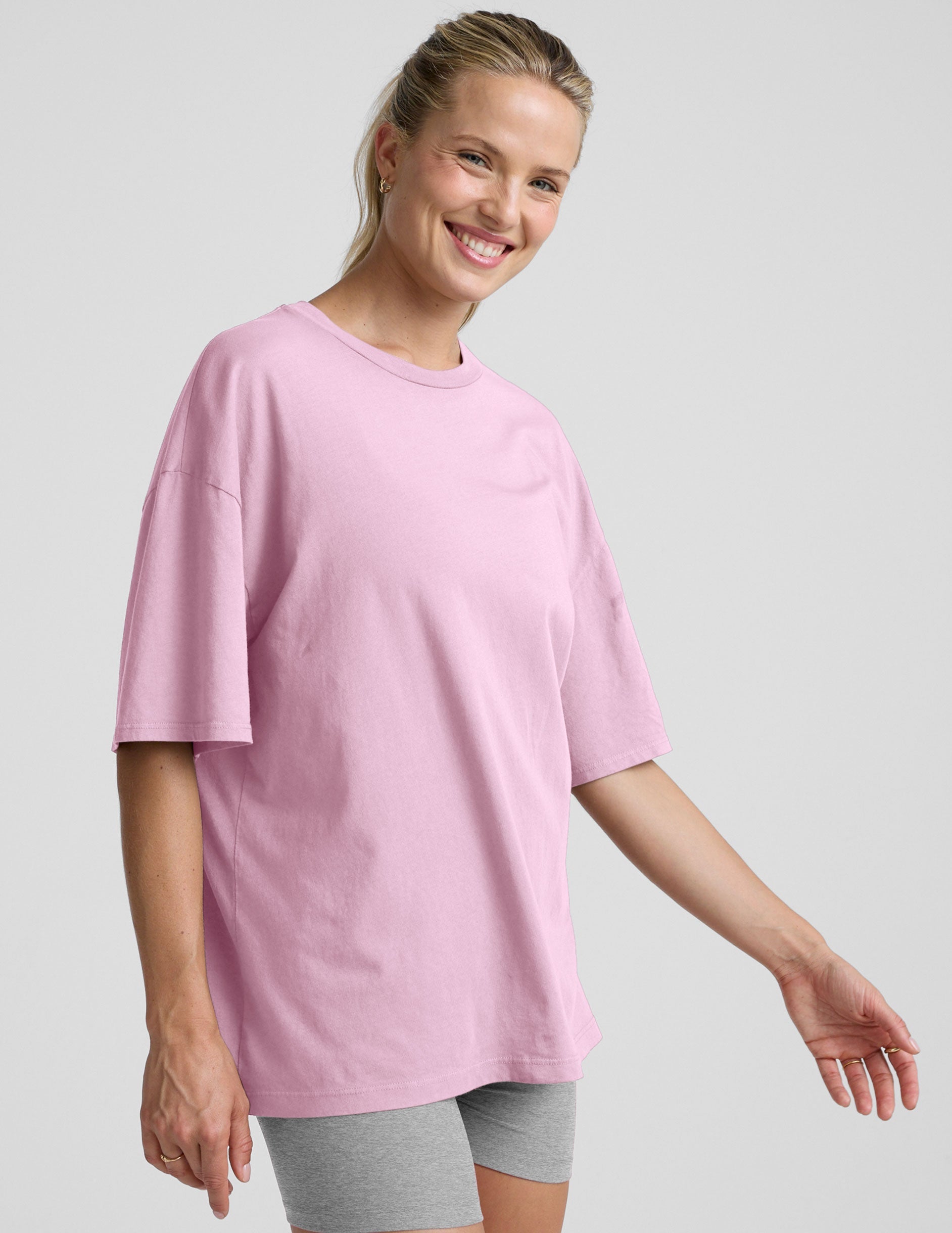 model wearing a pink oversized cotton t-shirt and grey biker shorts against a plain background.