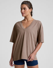 model wearing a brown oversized v-neck top and blue shorts on a plain background.
