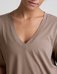 model wearing a brown oversized v-neck top and blue shorts on a plain background.