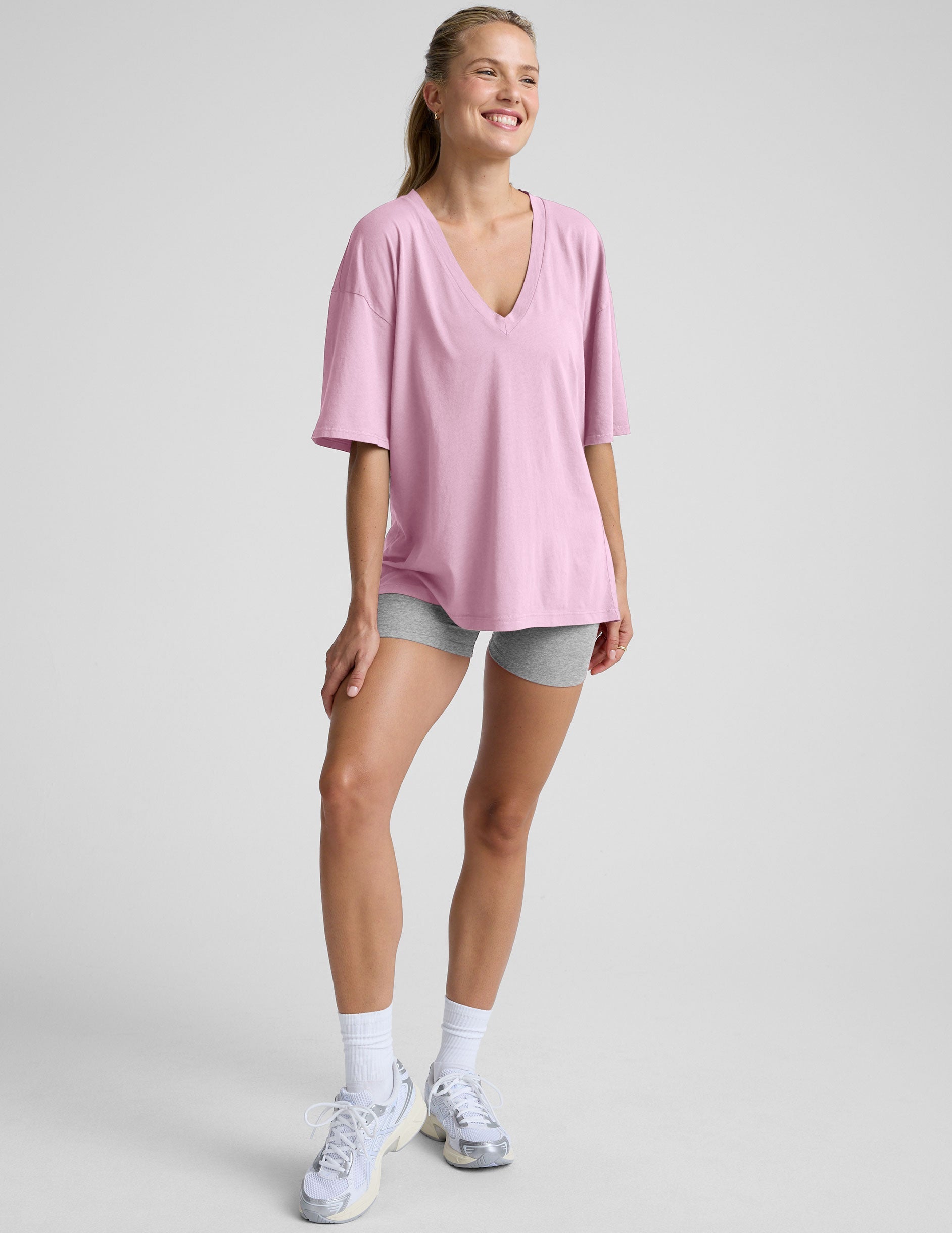 model wearing a pink oversized v-neck top and gray shorts on a plain background.