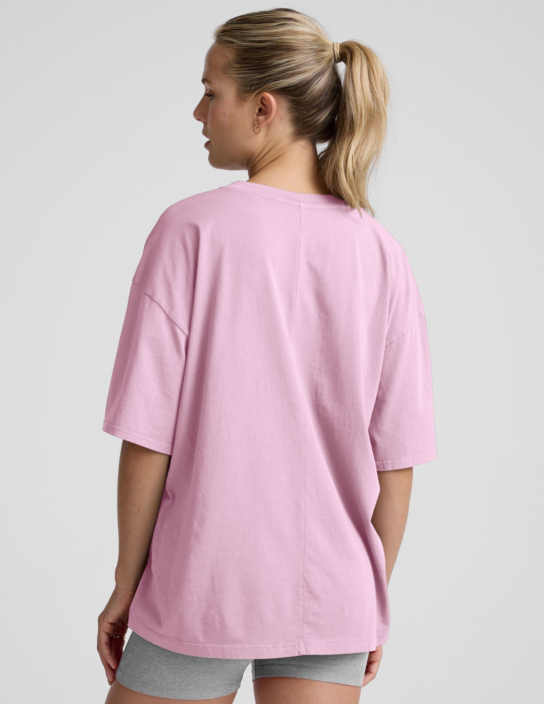 model wearing a pink oversized v-neck top and gray shorts on a plain background.