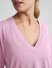 model wearing a pink oversized v-neck top and gray shorts on a plain background.