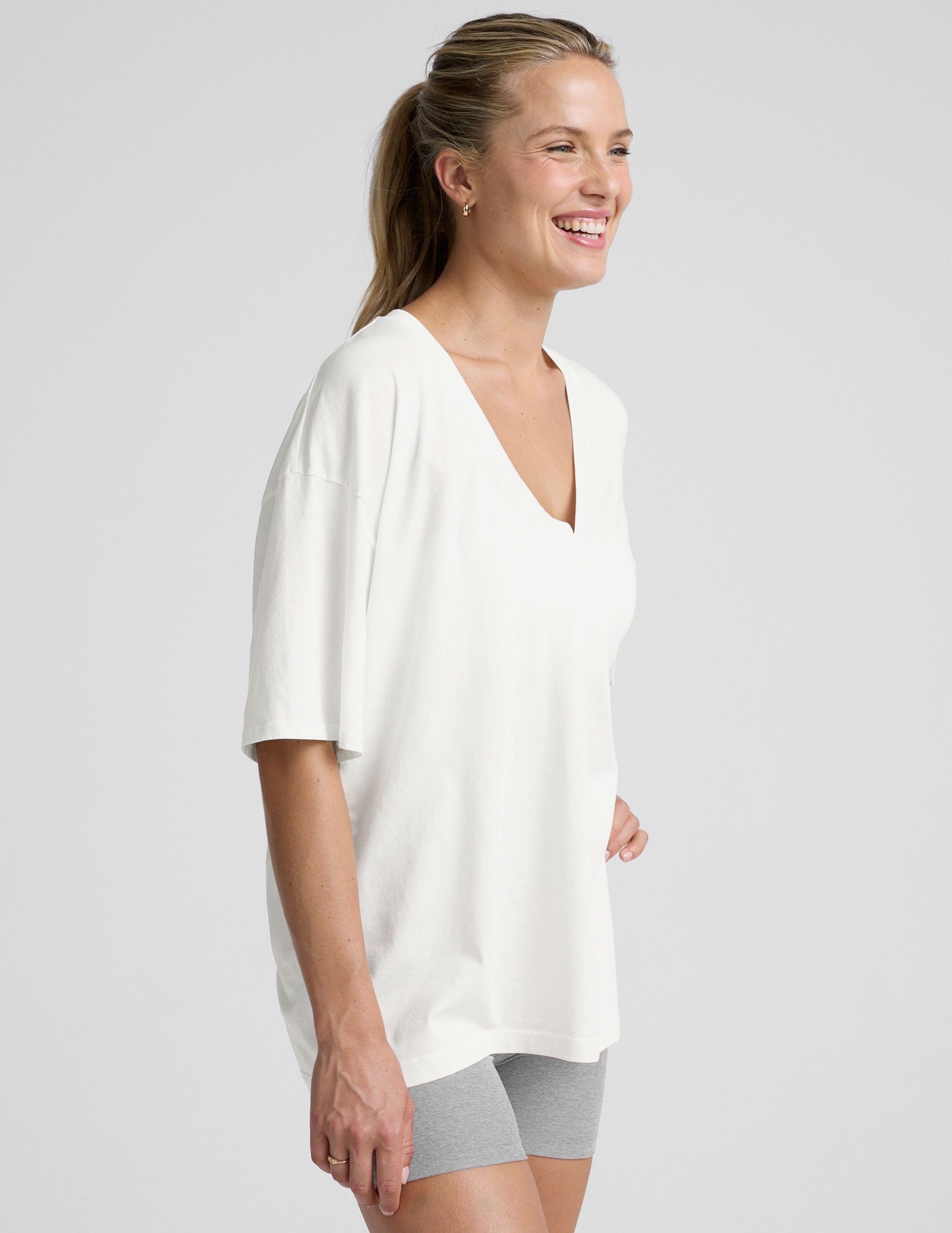 model wearing a white oversized V-neck top and gray shorts on a light background.