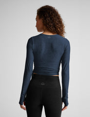 Woman wearing a blue long-sleeve wrap top and black leggings on a plain background.