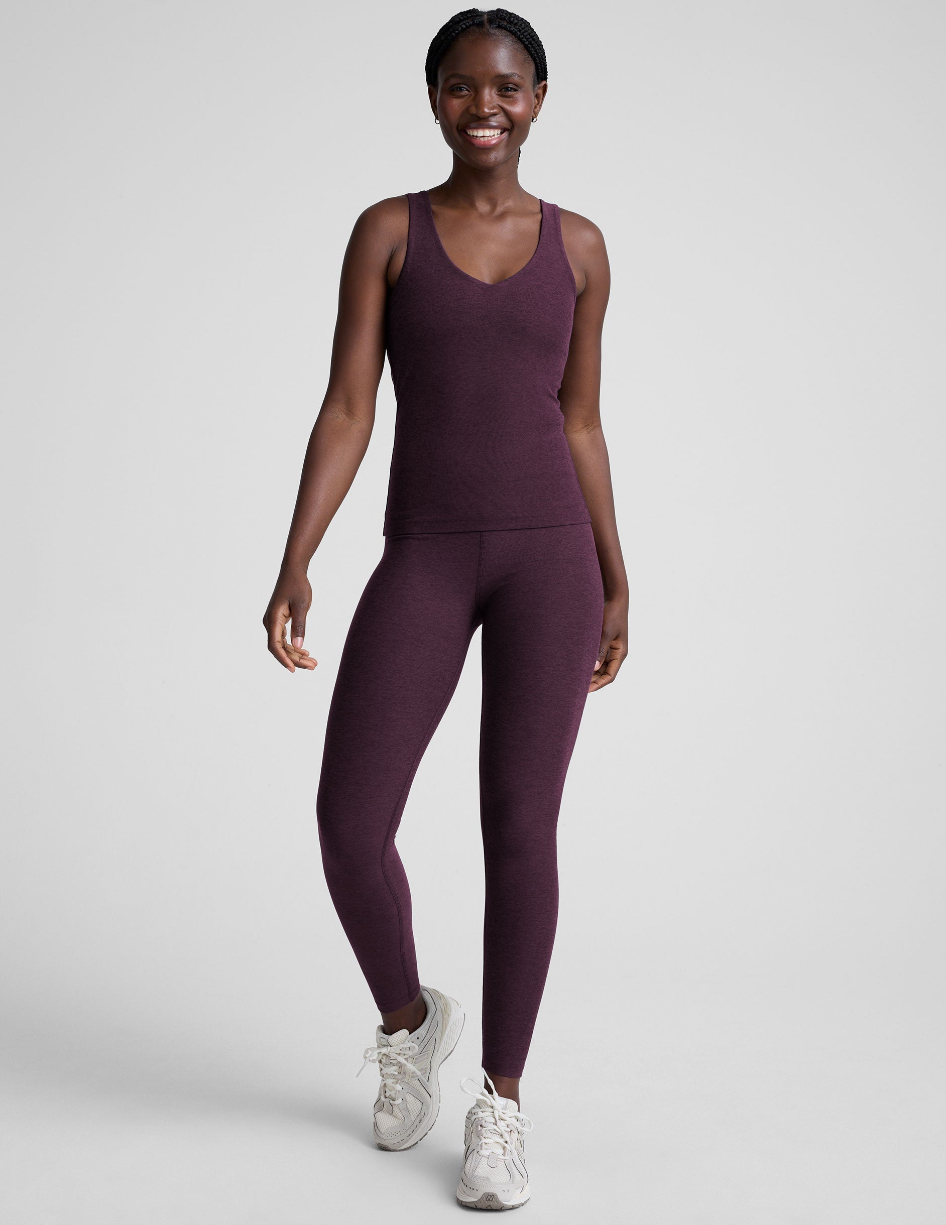 woman wearing a purple tank top and leggings on a light gray background.