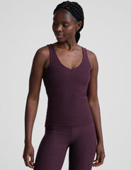 woman wearing a purple tank top and leggings on a light gray background.