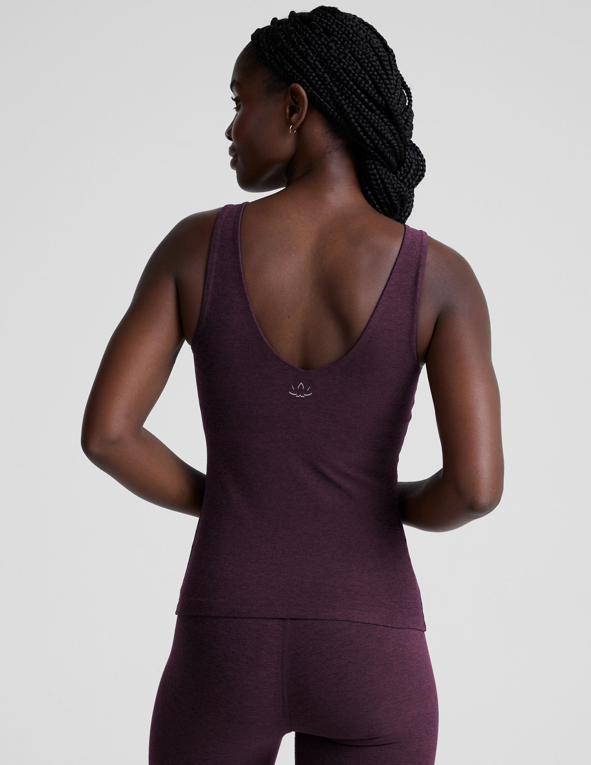 woman wearing a purple tank top and leggings on a light gray background.